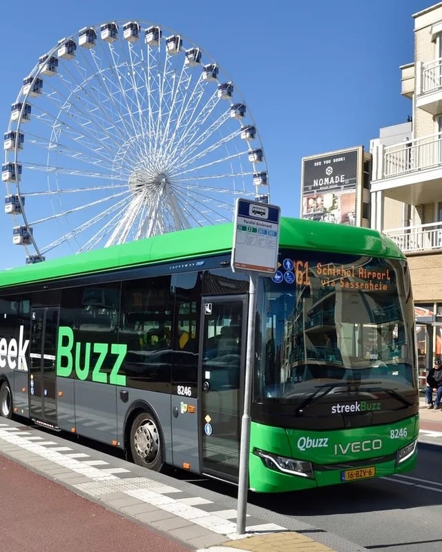 Een groene streekbus staat stil bij een halte in Katwijk. De bus staat voor een casino en een reuzenrad.