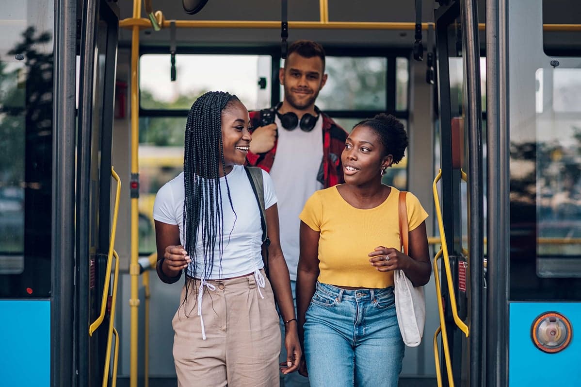 Drie jongeren stappen lachend uit een bus en voeren een gesprek.