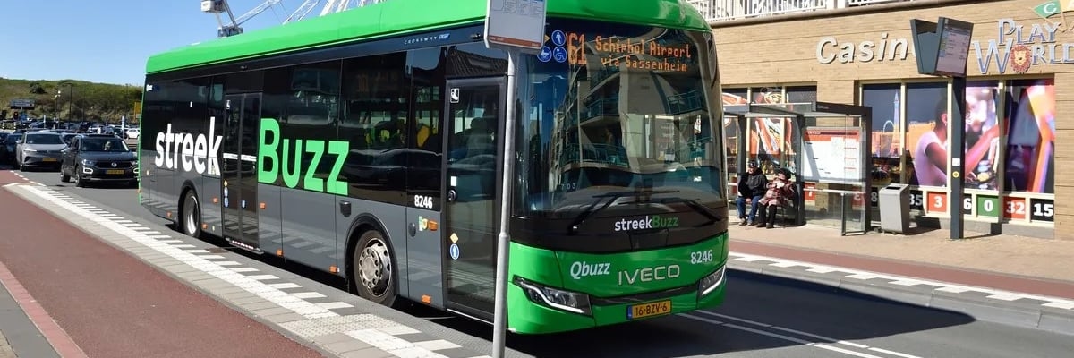 Een groene streekbus staat stil bij een halte in Katwijk. De bus staat voor een casino en een reuzenrad.
