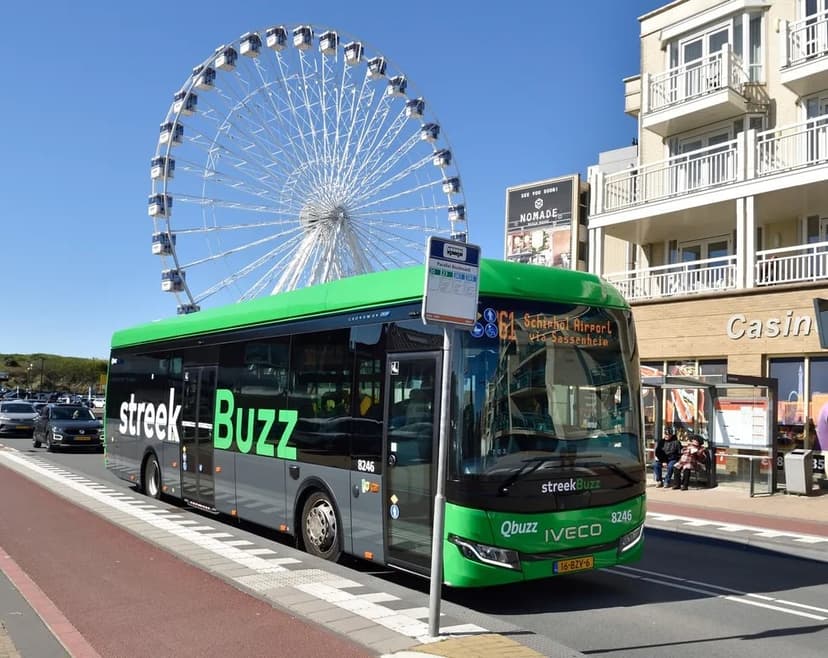 Een groene streekbus staat stil bij een halte in Katwijk. De bus staat voor een casino en een reuzenrad.