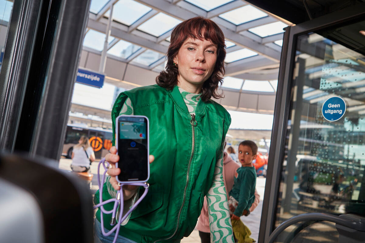 Reiziger stapt in bus en laat mobiele betaalpas zien bij het inchecken